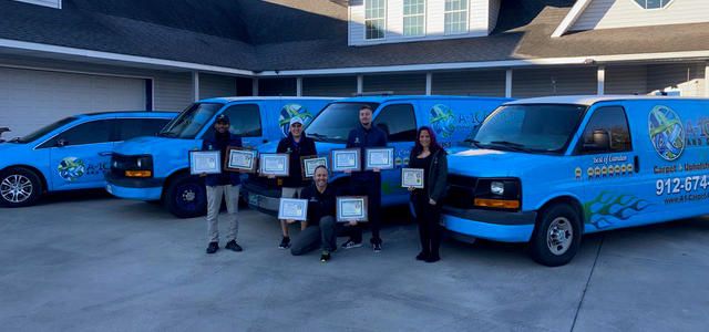Three A-1 Carpet Care vans in a driveway, with the crew holding Best of Camden awards